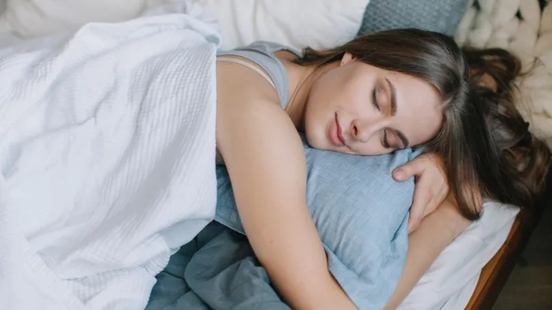 A woman resting peacefully in bed in soft morning light, with an empty coffee mug on the bedside table