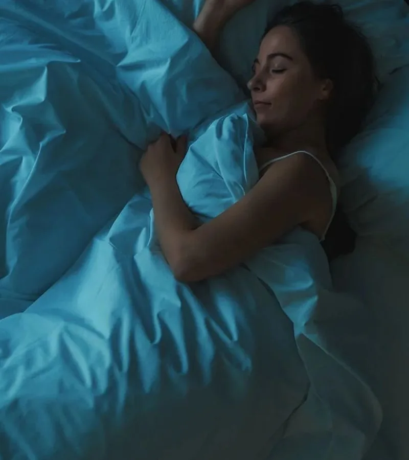 A woman lying awake in a bedroom lit by soft blue light