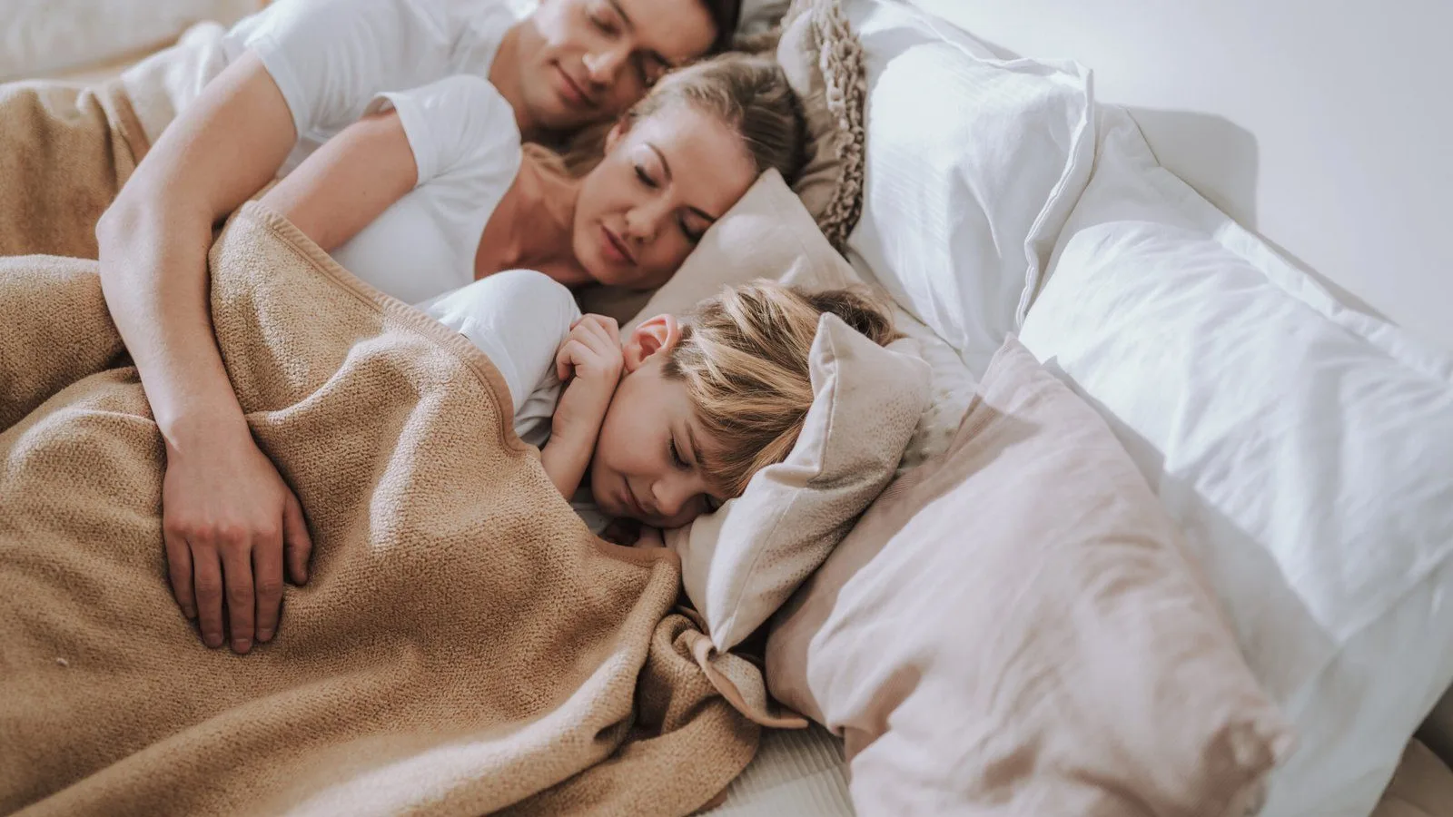 Family snuggled together, asleep under a light blanket