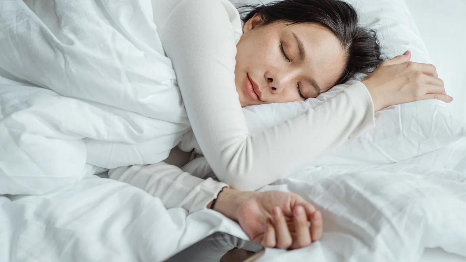 Woman resting in bed with white bedding in morning light